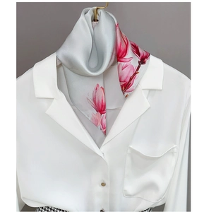 Macro shot of faux silk scarf with pink magnolia prints draped on a white shirt suit