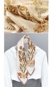 Macro view of silk satin scarf featuring yellow sunflower prints and brown hemmed edges