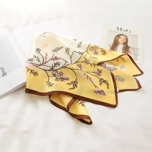 Elegant yellow silk scarf with floral patterns displayed on white bedding with books