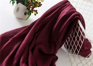 Detail of burgundy linen scarf draped over white wire basket with cozy home decor