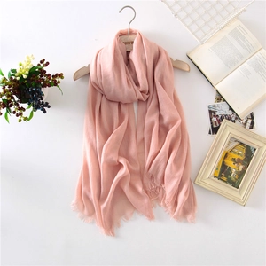 Detail of light pink linen scarf with delicate tassels hanging on a wooden hanger