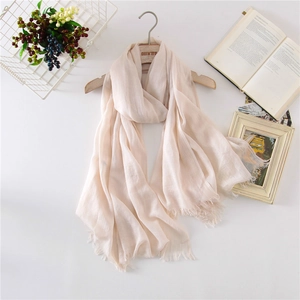 Detail of light beige cotton linen scarf featuring soft frayed edges and breathable texture