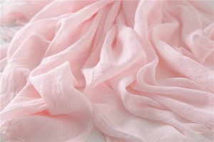 Detail of light pink linen scarf featuring soft fabric texture and fringe tassel edges