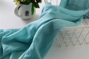 Detail of light blue cotton linen scarf texture draped over a white metal wire basket