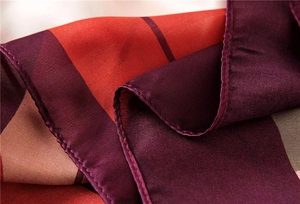 Detail of silk-like scarf featuring burgundy and orange stripes with fine rolled edges