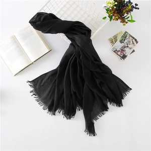 Detail of a black linen cotton scarf with frayed edges displayed on a vintage white basket