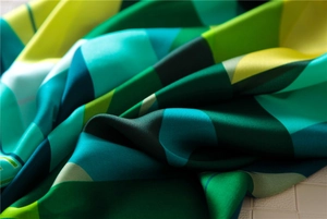 Macro detail of a soft satin scarf with green and blue geometric color block patterns