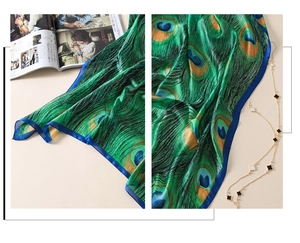Vue détaillée du motif plumes de paon sur un foulard en satin soyeux vert émeraude et bleu