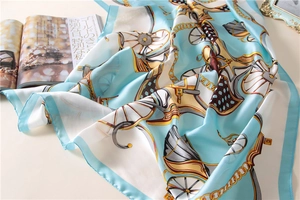 Detailed close-up of light blue silk scarf with golden chain and horse carriage patterns