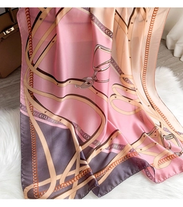 Detail of silk scarf with chain pattern on plush rug next to leather handbag