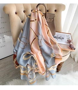 Close-up of elegant silk scarf with chain print draped over a beige leather chair