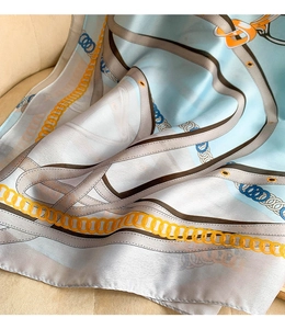 Detailed close-up of light blue silk scarf featuring gold chain and brown belt print pattern
