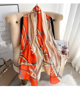 Detail of long orange and beige chain print silk scarf draped over a chair