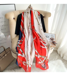 Detail of elegant silk scarf with red equestrian chain pattern draped over an armchair