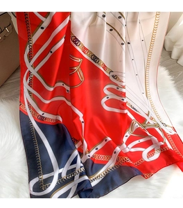 Close-up of elegant chain and belt print on red, white, and navy blue silk scarf fabric