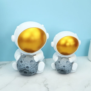 Detail of white astronaut piggy bank figurines with golden visors and grey moon textures