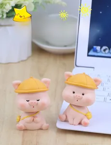 Close-up of two cute pink shaking head pig ornaments with yellow hats on a desk