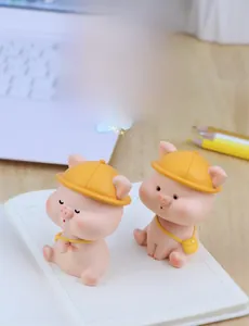 Close-up of two pink resin shaking head pig figurines with yellow hats for car decor