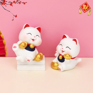 Macro shot of two white lucky cat resin figurines with golden ingots and bells