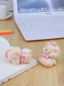 Detail of two pink resin cartoon pig figurines on a desk with blurred office background