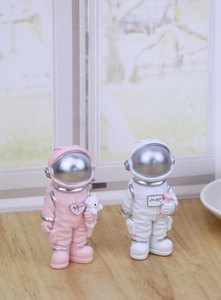 Close-up of pink and white astronaut figurines with silver details on wood surface