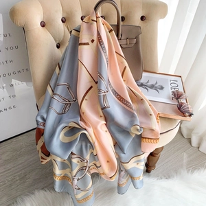 Elegant chain print silk scarf in pink and blue draped over a handbag on a chair