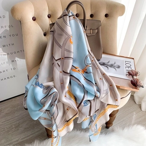 Elegant long silk scarf with blue horse chain print draped over a beige armchair