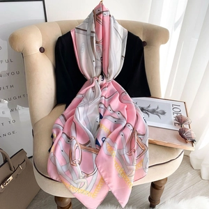 Pink and white silk scarf with golden chain horsebit print draped on a vintage chair