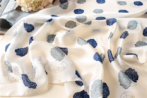 Close-up of silk scarf showing navy rose pattern on cream fabric with satin finish