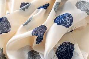 Detailed view of cream silk scarf featuring navy blue and grey rose floral patterns