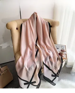 Detailansicht eines rosa Seidenschals mit Schleifenprint und schwarzen geometrischen Kanten