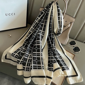 Black and white plaid silk scarf draped over a beige handbag in a luxury indoor setting