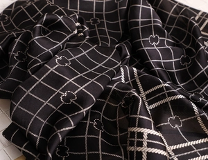 Detailed close-up of a black satin scarf with white rope plaid patterns and a silky texture
