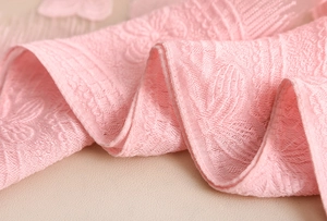 Dettaglio macro della sciarpa in pizzo rosa con ricami floreali 3D e bordi ondulati