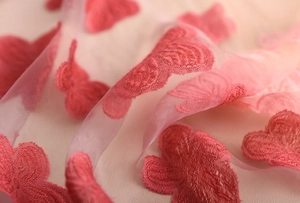 Dettaglio ravvicinato della sciarpa rosa sfumata con eleganti ricami a farfalla rossa
