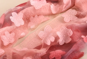 Dettaglio ravvicinato della sciarpa in pizzo rosa sfumato con eleganti ricami floreali