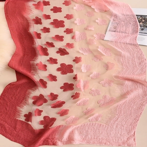 Dettaglio della sciarpa in pizzo sfumato rosso e rosa con ricami floreali e frange