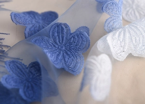 Dettaglio ravvicinato di ricamo floreale 3D blu e bianco su tessuto velato in pizzo