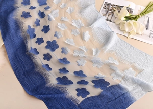 Dettaglio di sciarpa in pizzo mesh con ricamo 3D blu sfumato e frange sottili