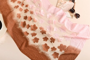 Dettaglio dell'elegante sciarpa in pizzo con applicazioni floreali e bordi con nappe