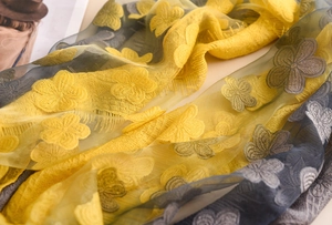 Dettaglio macro del ricamo floreale in pizzo giallo e grigio sulla sciarpa leggera velata