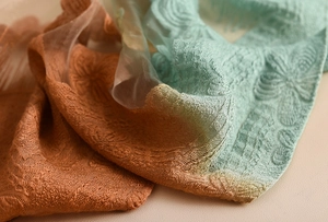 Dettaglio di sciarpa in pizzo floreale con sfumatura arancione-verde e motivo jacquard