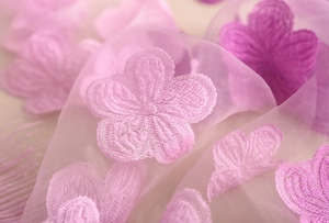Dettaglio macro del ricamo a rose su tulle sfumato rosa e viola di pizzo