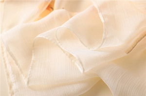 Detailed close-up of cream-colored pleated silk scarf fabric with fine vertical texture
