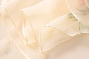 Close-up of cream floral silk scarf fabric showing delicate leaf print and rolled hem