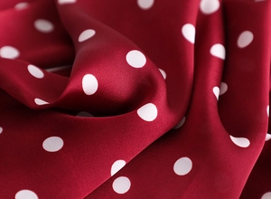 Gros plan détaillé du tissu en satin bordeaux brillant avec motif à pois blancs