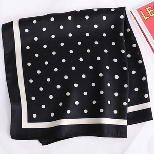 Détail d'un foulard en soie noir à pois blancs avec une bordure contrastée chic