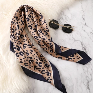 Detail of leopard print silk scarf with navy blue borders on white marble background