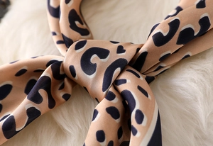 Macro detail of leopard print silk scarf with satin luster and blue border on white faux fur