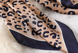 Macro shot of leopard print silk scarf with deep blue border and satin texture detail